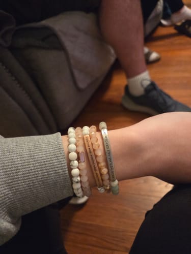 Customer's wrist with a stack of bracelets, including the pink crystal bracelet and other beaded styles.