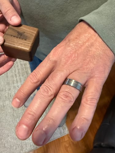 Reviewer wearing The Lancelot ring, a brushed tungsten band with a rose gold inlay, while holding the wooden ring box.