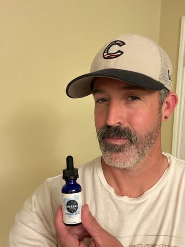 Reviewer in a cap holding up a small blue bottle of Meraki Blu Methylene Blue.