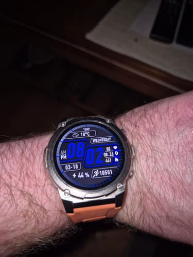 Customer's smartwatch with a silver case and orange band on their wrist. The digital face displays time, date, and health metrics.
