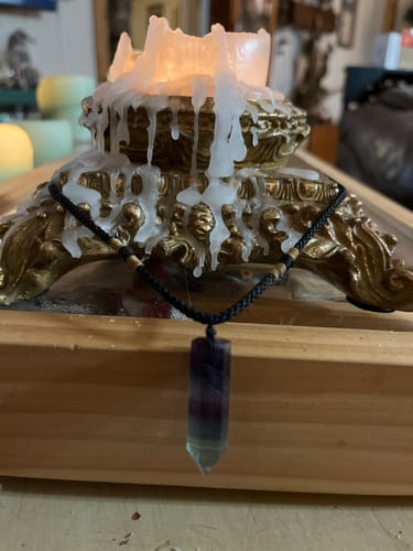 Customer's crystal necklace with a colorful pointed pendant on a black cord, displayed before a lit candle.