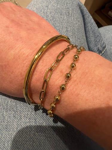 Close-up of a reviewer's wrist, showing the Classic Oval Bangle stacked with two other gold bracelets.