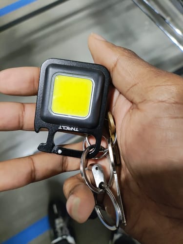 Customer holding the black TNRCLT mini flashlight keychain in their hand, attached to a set of keys.