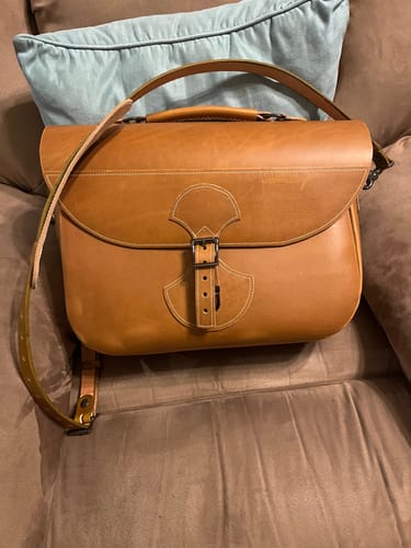 Reviewer's finished tan leather Saddlebag Satchel resting on a couch, showing the front buckle closure.
