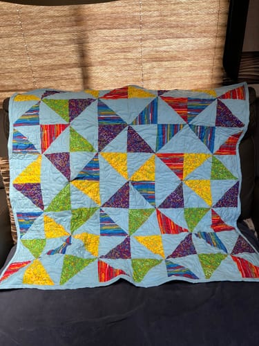 Customer's colorful first quilt made with their Janome sewing machine, featuring a vibrant triangle pattern.