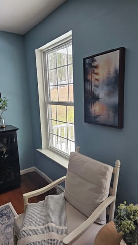 Customer's Misty Lake Wall Art hanging on a blue wall next to a window and chair.