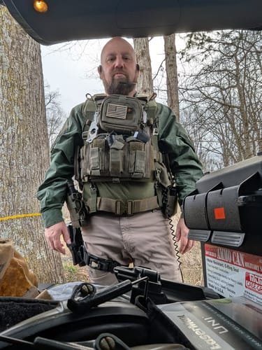 Reviewer in full tactical gear outdoors, wearing the XCOR PRO EXCHANGE earbud in their right ear.