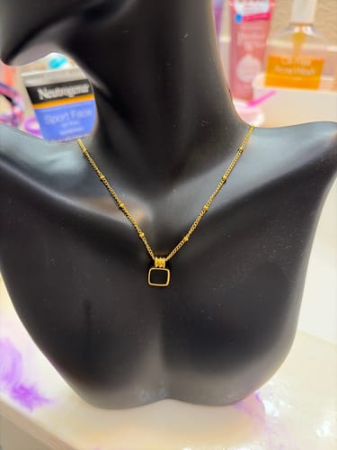 A customer's Lucia Black Pendant Necklace with a delicate gold chain, displayed on a black bust.