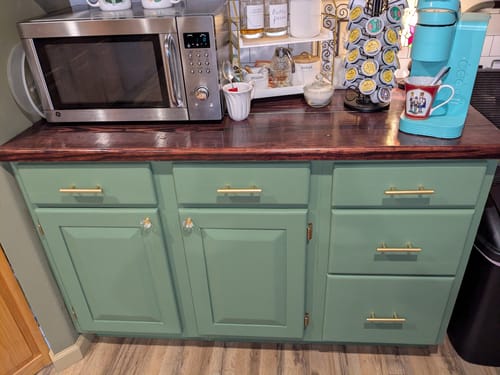 Customer's kitchen base cabinets painted a rich green with One Step Paint, shown below a dark wood countertop.