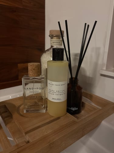 Customer's Body Serum on a wooden bath caddy, placed with other toiletries.