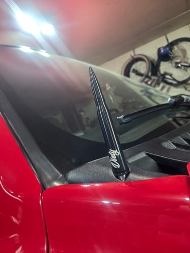 Close-up of a customer's black 50 Cal. Bullet Antenna installed on a red truck by the windshield.