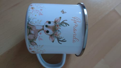 Bewertung eines Kunden: Personalisierte Emaille-Tasse mit Reh-Motiv und dem Namen 'Amanda', die auf der Seite auf einem Tisch liegt.