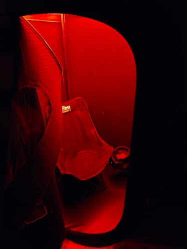 A customer's Sauna Pod, shown in a dark room with its interior glowing red.