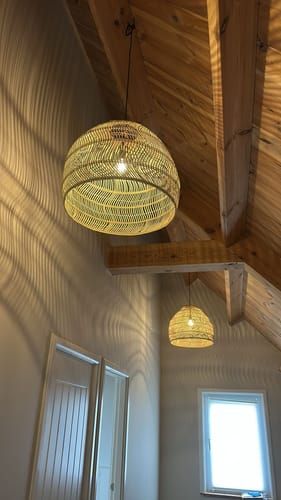 Klant toont twee HKliving Wicker hanglampen in een hoge vide, die een golvend lichtpatroon op de muur werpen.