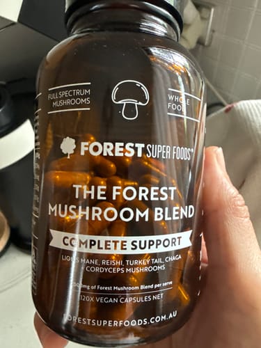 Customer's hand holding a brown bottle of The Forest Mushroom Blend capsules, with the capsules visible inside.