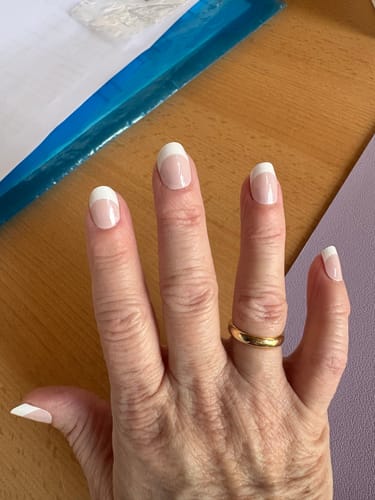 Die Hand eines Rezensenten mit den aufgetragenen 'Soft French' UV Gel Wraps, die breite weiße Spitzen zeigen.