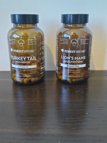 Customer's bottle of Turkey Tail Mushroom capsules on a wooden table, next to a bottle of Lion's Mane Mushroom.