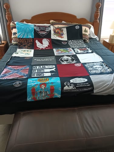 Customer's colorful Premium T Shirt Quilt with a black border, spread across a bed with a wooden headboard.