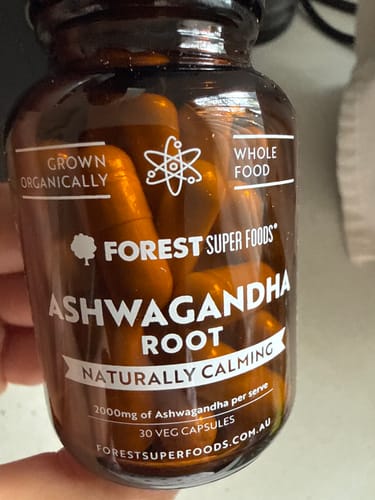 Reviewer holding a bottle of Mini Pure Ashwagandha Root Capsules, showing the label and capsules inside.