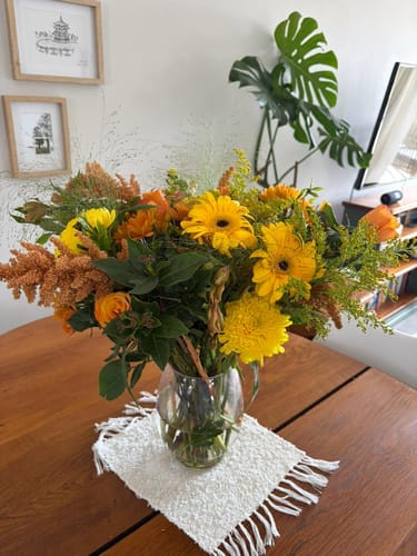 Customer's Sparkling Orange Bouquet with bright yellow and orange flowers in a vase on a table.