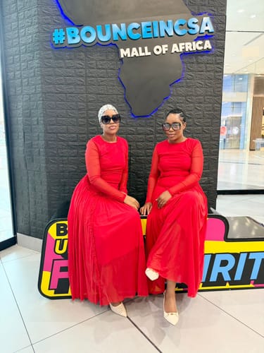 Two customers wearing matching red elegant mock-neck maxi dresses in a mall.