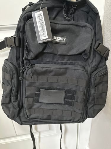 Customer's new black 80Eighty Commando Raven Backpack hanging on a door with tags still attached.