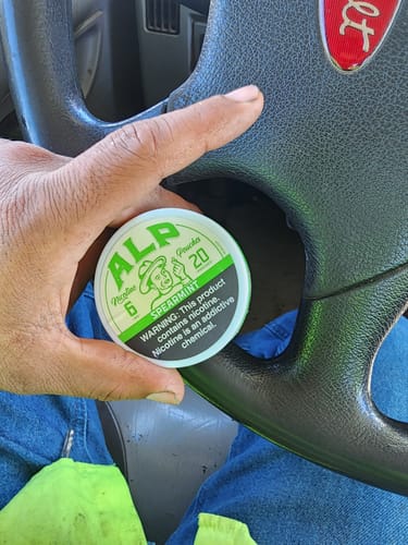 Customer holding a round, green tin of Spearmint Nicotine Pouches in a vehicle.
