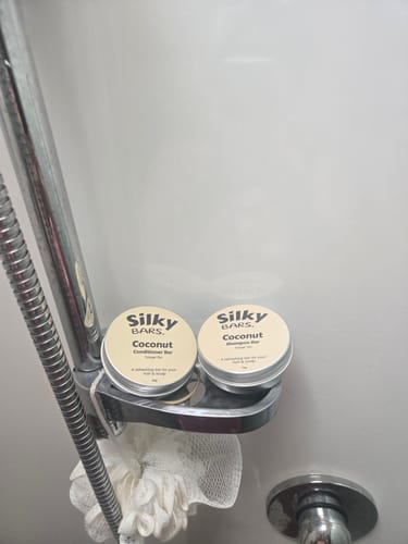 Customer's Coconut Oil Conditioner Bar in its round tin, stored with a shampoo bar in a shower caddy.