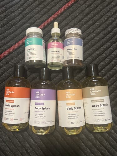 Customer's collection of Her Fantasy Box products, including various body oils and supplements, arranged on a dark textured surface.