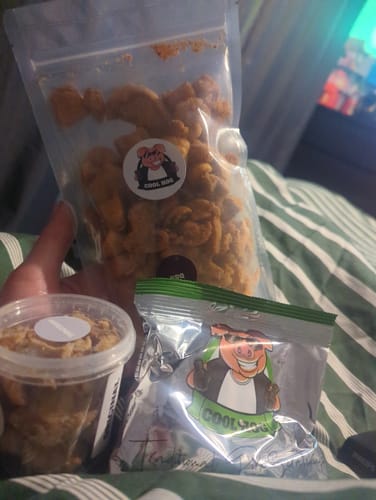 A reviewer holds the three items from The Piggy Bank Bundle: a large refill bag, a taster tub, and a small foiled packet.