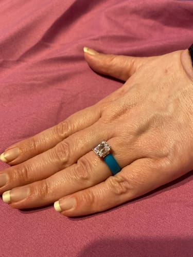 Customer's hand wearing the Silicone Ring, showing the teal band and large emerald-cut CZ stone.