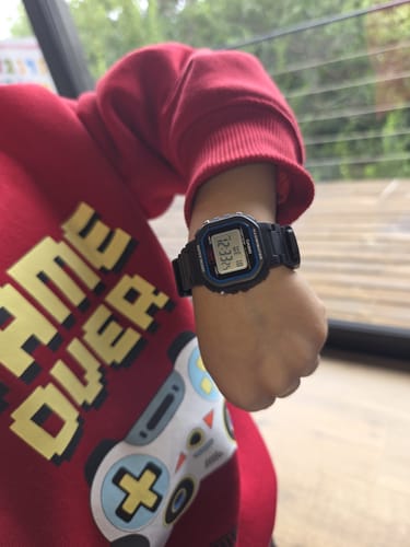 Cliente muestra el pequeño reloj Casio Vintage negro en la muñeca de un niño que lleva un suéter rojo.