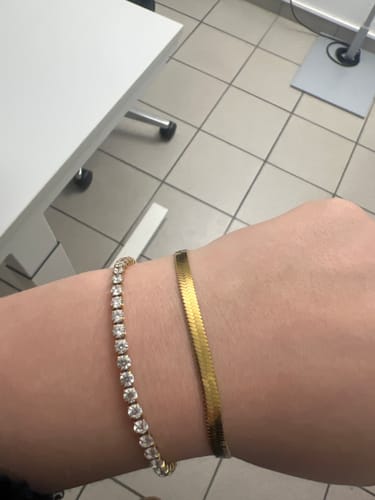Eine Kundin trägt das glänzende Tennisarmband am Handgelenk neben einem weiteren goldenen Armband.
