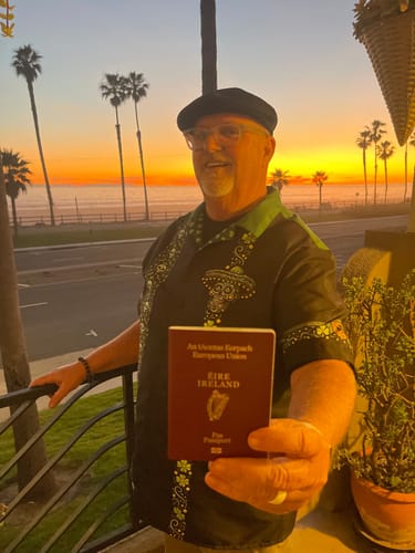 Reviewer wearing the San Patricio Calavera Guayabera shirt, holding an Irish passport in front of a beach sunset.