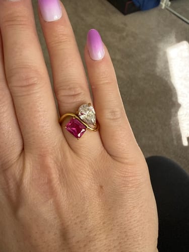 Customer's hand wearing the Navae Birthstone Ring, showing the pink radiant-cut and clear pear-cut stones.