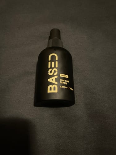 Customer's black bottle of Based Bodyworks Sea Salt Spray resting on a dark fabric.