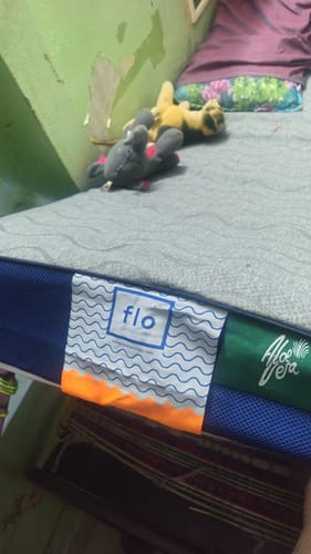 Customer's grey Flo Aloe Vera mattress protector fitted on a mattress, with brand labels visible on the side.