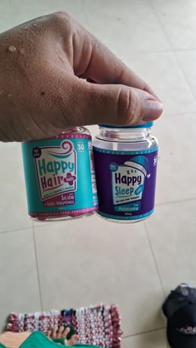 Cliente segurando um pote de Happy Hair e um pote de Happy Sleep sobre um piso de cerâmica.