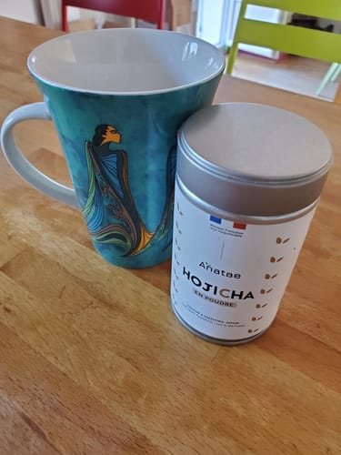 Photo d'un client de la boîte de THÉ HOJICHA BIO à côté d'une grande tasse sur une table en bois.
