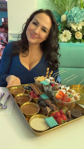 Reviewer with full, dark wavy hair smiling while sitting at a table in a restaurant.