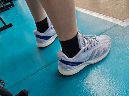 Customer wearing the light blue adidas Courtflash Pickleball Shoes on a textured blue athletic court.