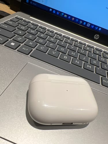 A reviewer's white charging case for the LOT Earbuds placed on a silver laptop.