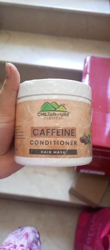 Customer holding a sealed, white tub of the Caffeine Conditioner Hair Mask indoors.