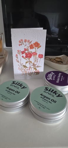 Customer's Argan Oil Shampoo Bar tin next to a conditioner tin and a thoughtful floral card on a table.