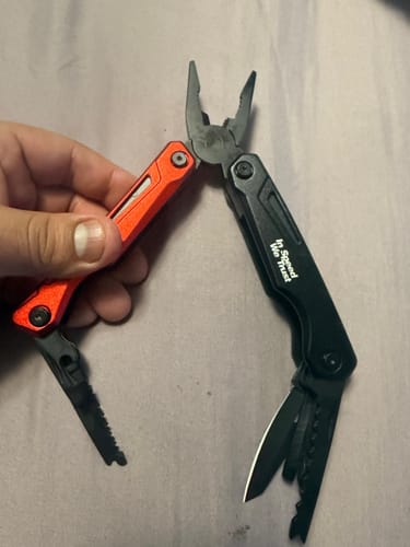 Customer holding the red and black multi-tool, which is open to show the pliers and other tools.