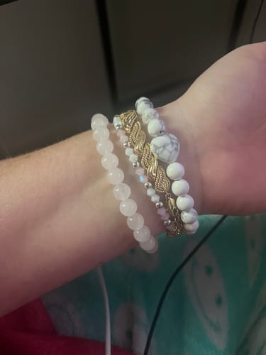 A customer's wrist wearing a stack of bracelets, including a white marbled crystal bracelet with a heart bead.