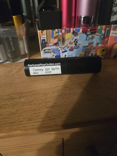 Reviewer's black travel spray bottle of Tommy Girl perfume on a wooden surface.