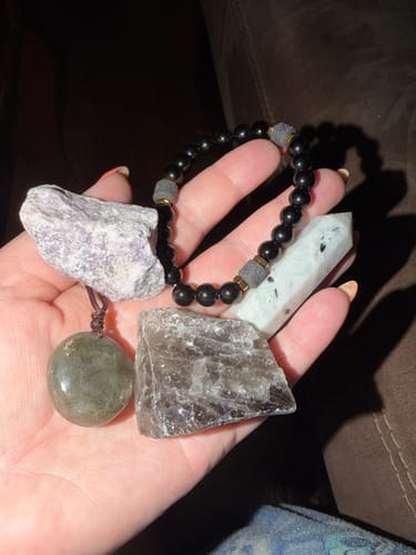 Customer's hand holding assorted crystals and jewelry from their AuraBloom Subscription Box.