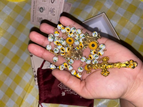 Customer's hand holding the handmade Sunflower-Inspired Rosary, showing its floral ceramic beads and gold crucifix.