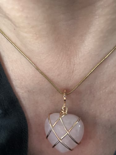 Reviewer wearing a necklace with a heart-shaped, pink crystal pendant wrapped in gold wire.